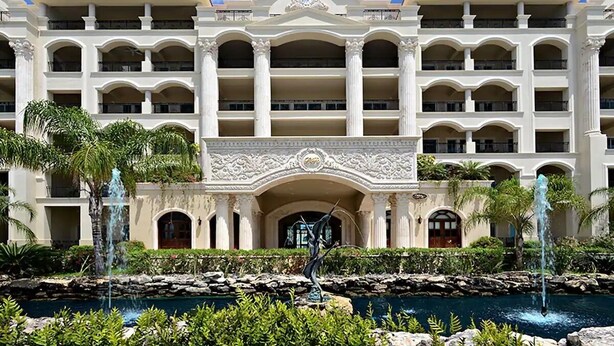 Un hotel de varios pisos con un patio central que presenta una fuente y palmeras.