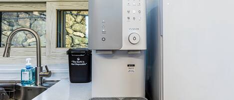 Una cocina moderna con dispensador de agua incorporado, un cubo de basura negro y un lavamanos de acero inoxidable.