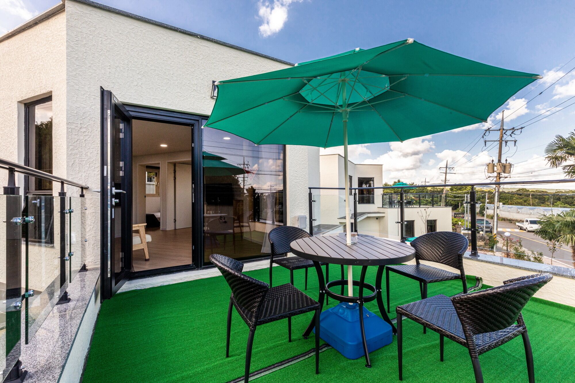 Varanda com guarda-sol verde, cadeiras de vime e porta de vidro que dá para o interior.