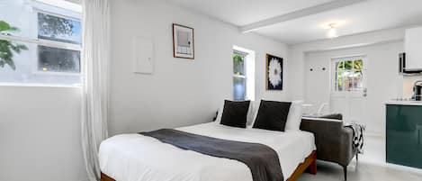 A modern bedroom with a large bed, a desk, and a view of the outside.