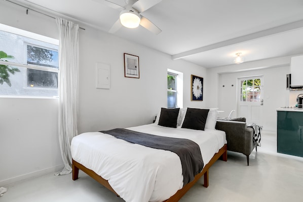 A modern bedroom with a large bed, a desk, and a view of the outside.