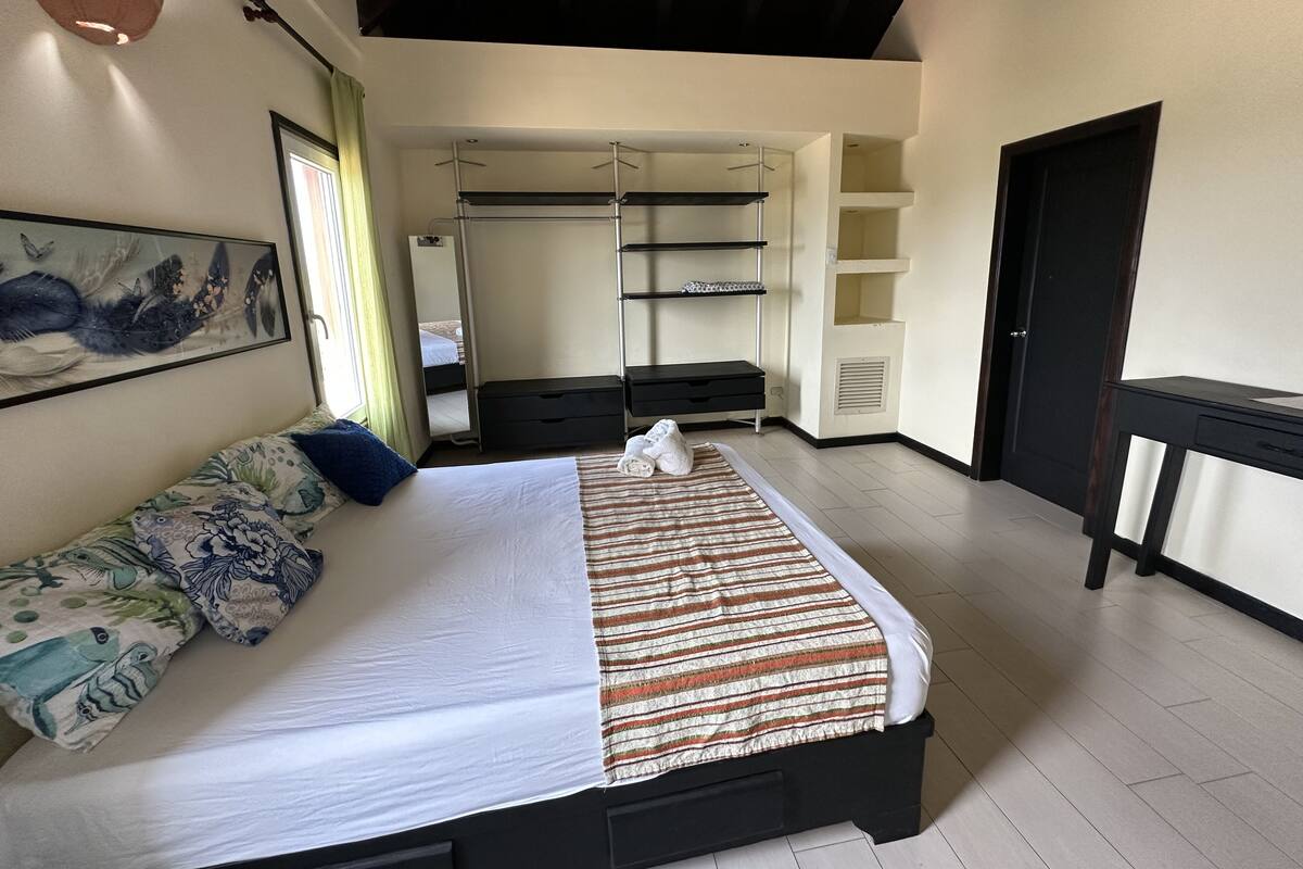 A bedroom with a bed, a dresser, a desk, a wardrobe, and a mirror.