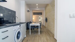 A compact kitchen with a washing machine, a dining area with a table and chairs, and a living space with a sofa and a TV. - VLC HOST - Fray Pedro A (Valencia)