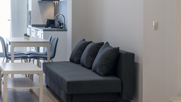 A modern hotel room with a grey sofa, a white bed, and a dining area with a table and chairs. - VLC HOST - Fray Pedro A (Valencia)