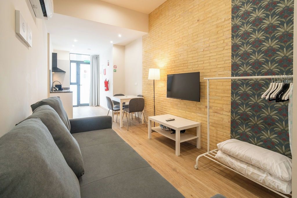 A modern living room with a sofa, a small table, a TV mounted on a brick wall, and a clothing rack.
