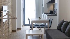 A modern hotel room with a bed, a dining table with chairs, a sofa, a kitchen area, and a view through the door. - VLC HOST - Fray Pedro A (Valencia)