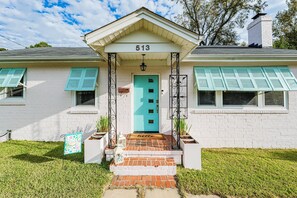 A two-story house with a white exterior and turquoise shutters, number 513, featuring a front porch with a 'hello' mat and a small garden area. - Charming Cottage, with pool… close to National Hills Masters Tournament.
 (North Augusta)