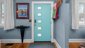 A teal door with a picture above it, a small table with a tray, and a coat rack with colorful items.