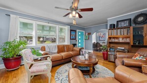 A living room with a brown leather sofa, a white armchair, a wooden coffee table, and a ceiling fan.