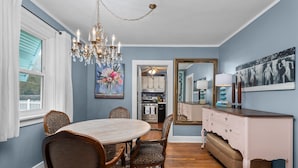 A dining room with a round table, chairs, a chandelier, a mirror, and a dresser.