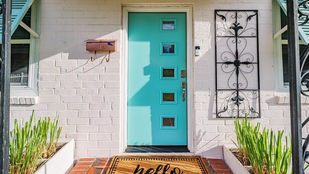 A turquoise door with a mailbox and a decorative metal gate, surrounded by white brick walls and green shutters.