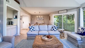 Ein Wohnzimmer mit einem hellblauen Sofa, einem Couchtisch und Blick ins Freie durch große Fenster.