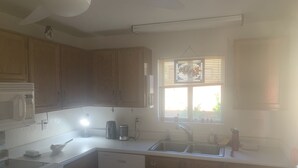 A kitchen with wooden cabinets, a microwave, a stove, a sink, and a window with blinds.