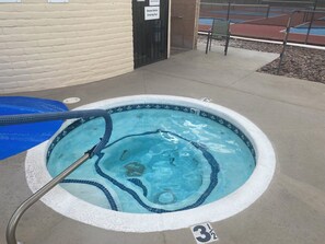 A small, tiled hot tub with a hose, a sign indicating a shower before entering the pool, and a number '3 1/2' on the ground.