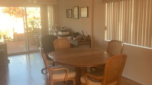 A dining area with a round table, four chairs, a ceiling fan, and a view through a glass door to an outdoor patio.