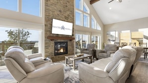 Un salón amplio con chimenea de piedra, sofás de cuero y ventanas grandes que ofrecen vistas al exterior.