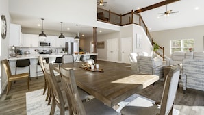 Amplia sala de estar con un gran comedor de madera, una cocina con electrodomésticos modernos y una escalera que conduce a un nivel superior.