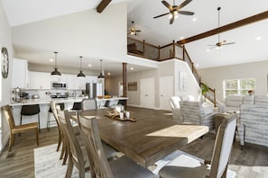 Un vaste espace de vie comprenant une grande table à manger en bois, une cuisine équipée d’appareils électroménagers modernes et un escalier menant à l’étage supérieur.