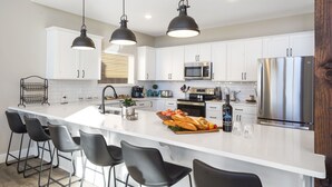Une cuisine moderne avec des meubles blancs, un réfrigérateur en acier inoxydable, un four à micro-ondes et un grand îlot central doté de tabourets de bar.