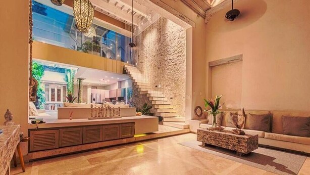 Un vestíbulo amplio con diseño moderno, que cuenta con una zona de estar central, una escalera y un gran ventanal con vistas a un jardín.