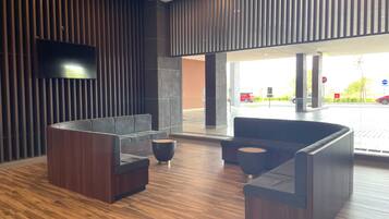 A modern lobby with dark wood flooring, a large sectional sofa, a round black coffee table, and a flat-screen TV mounted on the wall.