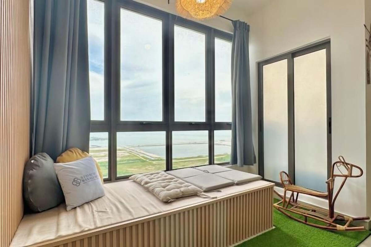 A room with a large window, a bed with pillows, a radiator, and a rocking chair.