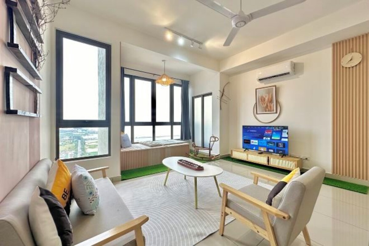 Een moderne woonkamer met een bank, salontafel en stoelen. Er is een televisie op een meubel, een plafondventilator en grote ramen.