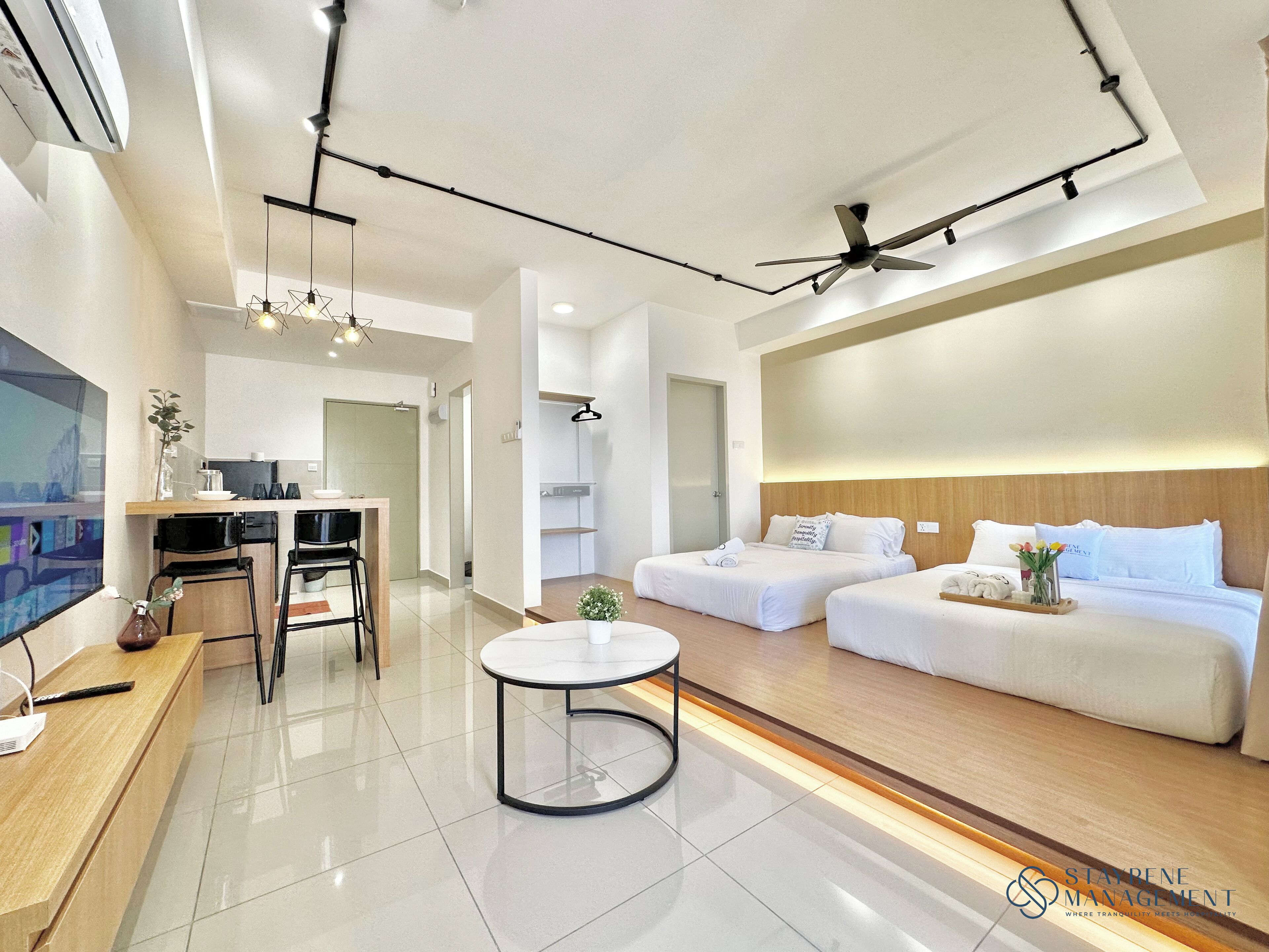 A modern hotel room with a kitchenette, two beds, a round table, and a ceiling fan.