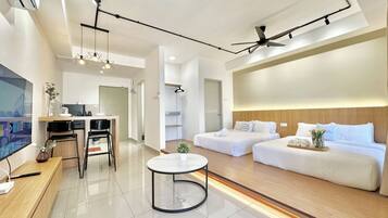 A modern hotel room with a kitchenette, two beds, a round table, and a ceiling fan.
