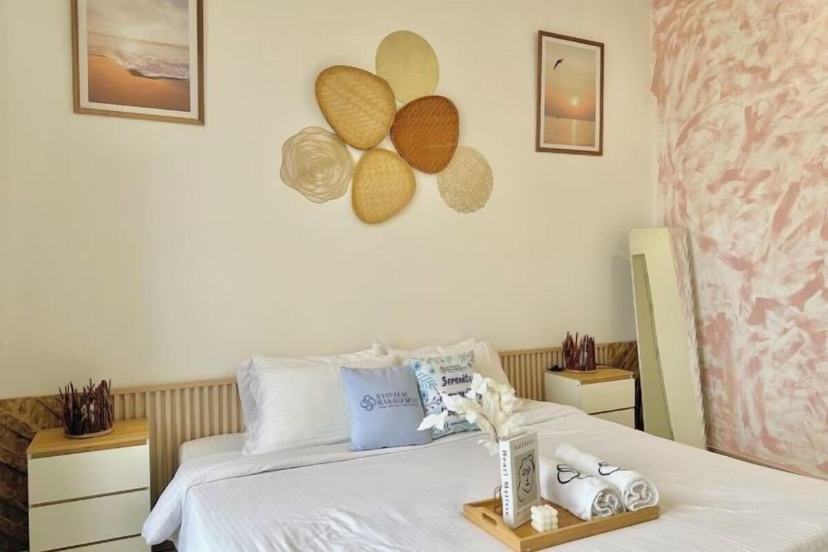 Habitación de hotel con una cama bien tendida, una instalación de arte en la pared y una mesita de noche con una bandeja de toallas.
