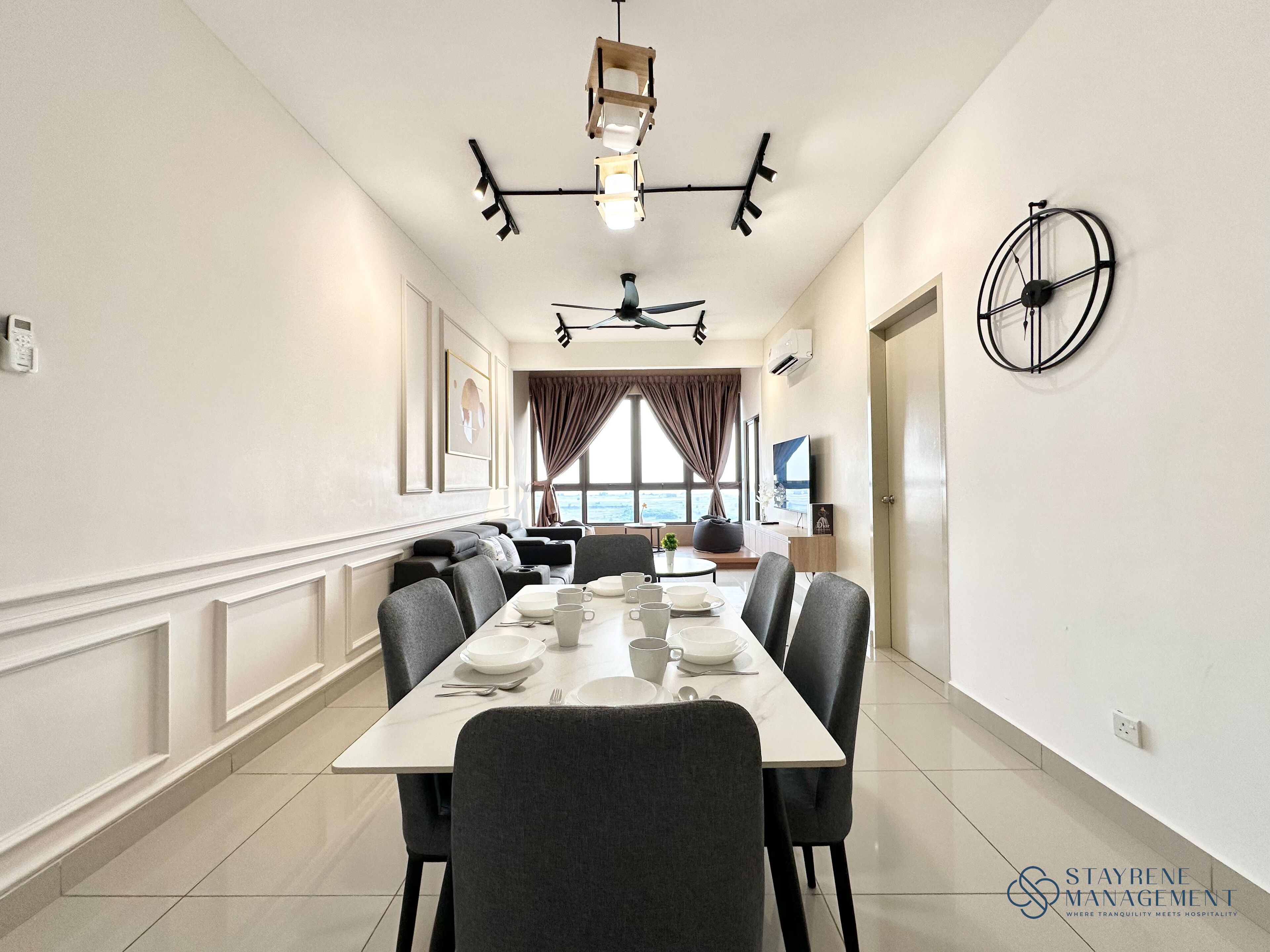 A dining area with a long table set for four, a ceiling fan, and a clock on the wall.
