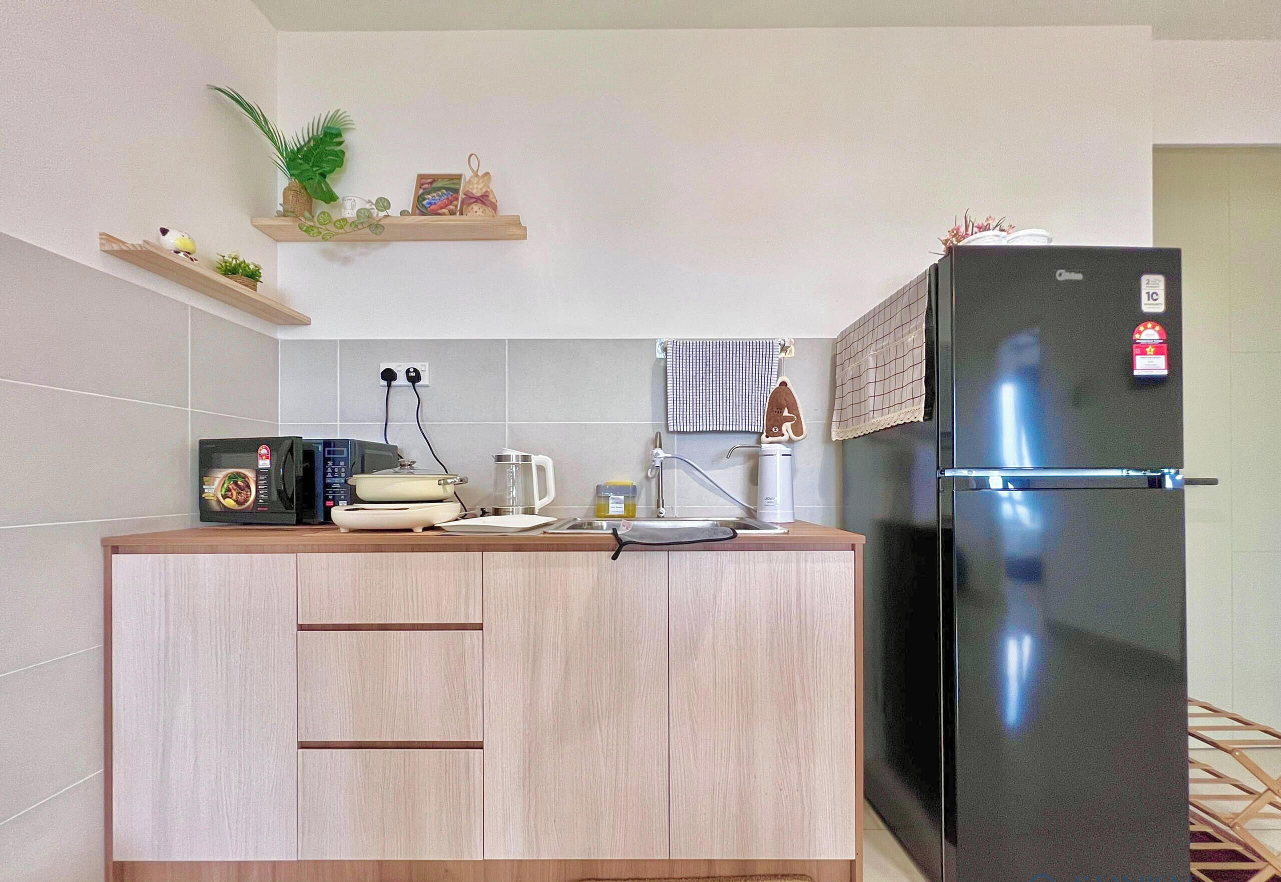 A kitchen with a black refrigerator, wooden cabinets, a microwave, and a kettle.