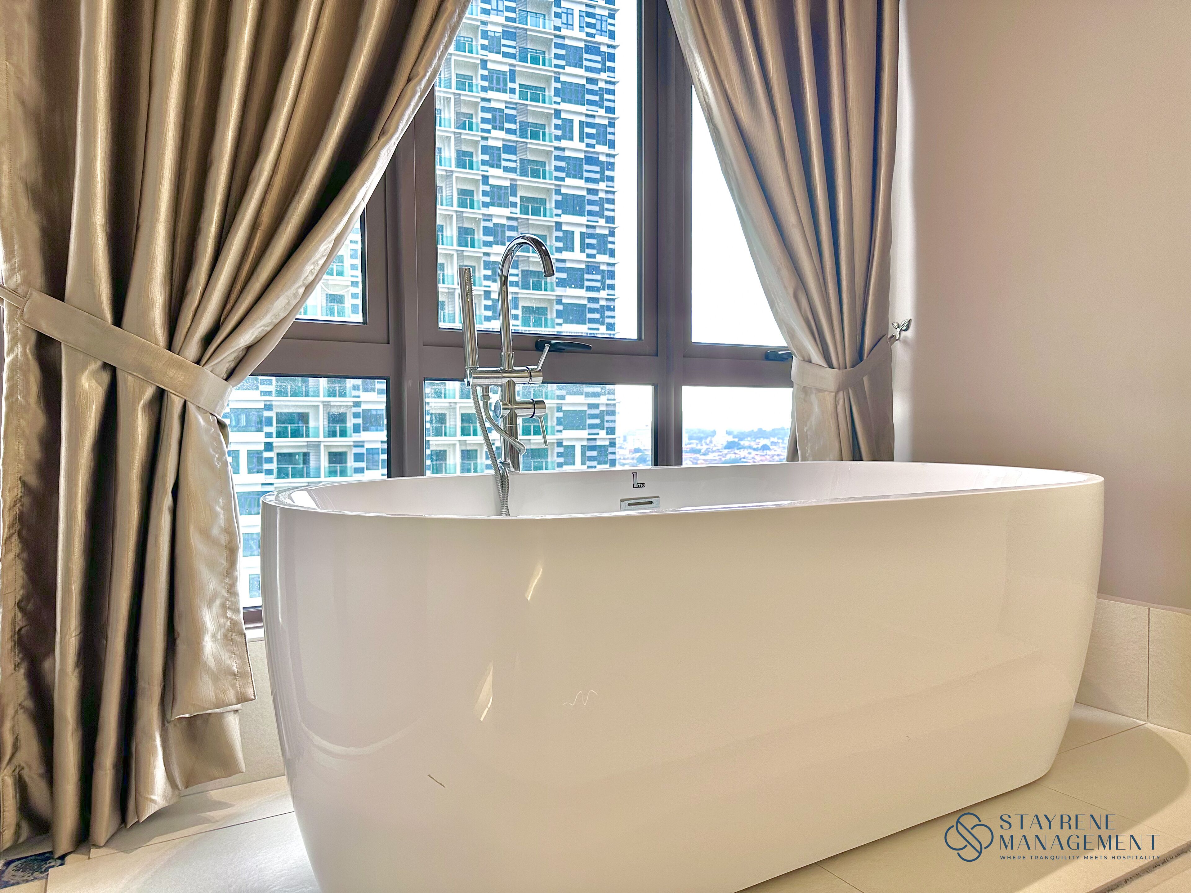 A modern bathroom with a freestanding bathtub, a window with curtains, and a view of a high-rise building.