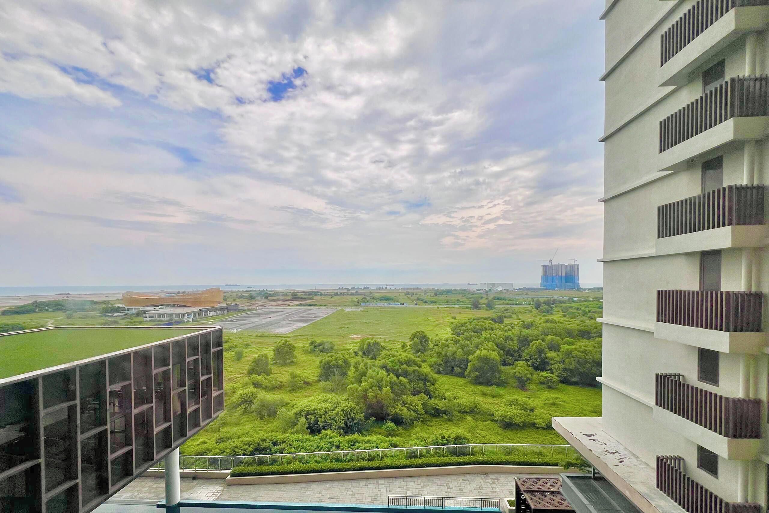 A high-rise building with a view of a green landscape and distant construction.