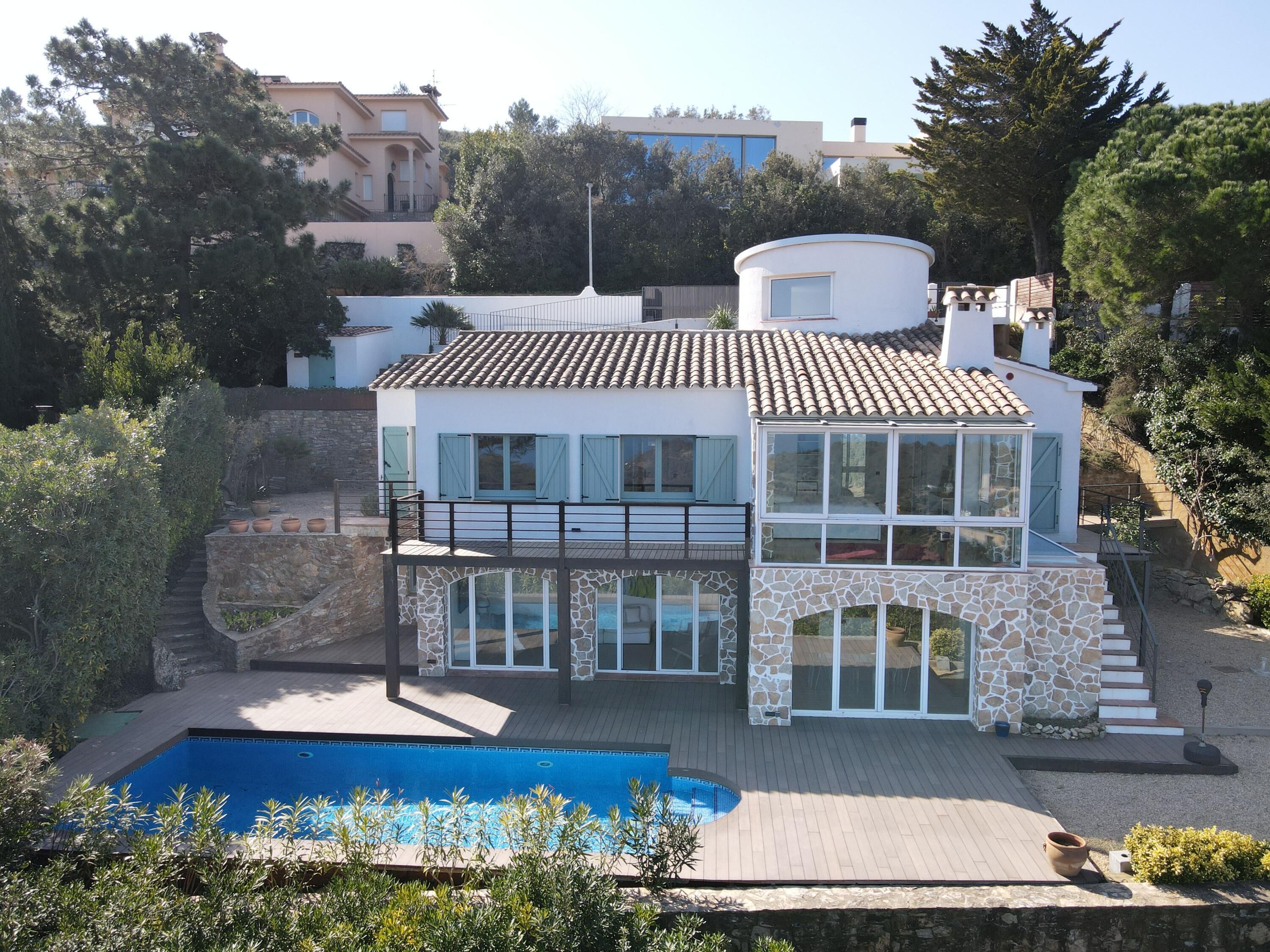 A modern two-story house with a swimming pool, stone walls, and a balcony.