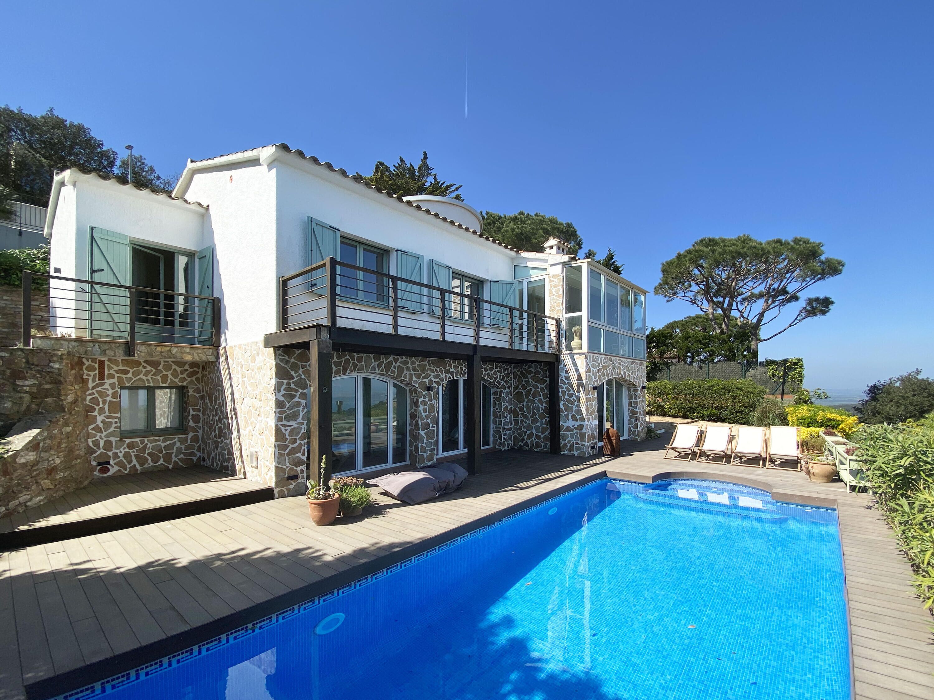 Ein zweistöckiges Haus mit Pool, Steinmauern und einem Balkon mit Geländer.