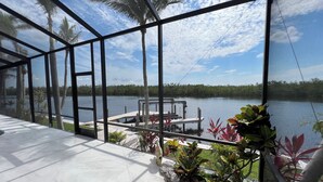 Vista desde una habitación con paredes de vidrio sobre un lago, con un muelle y palmeras a la vista.