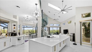 Una cocina amplia con una isla central, una escalera en espiral y grandes ventanales que ofrecen vistas al exterior.