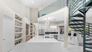 Una cocina moderna con armarios blancos, una isla central y una escalera en espiral.