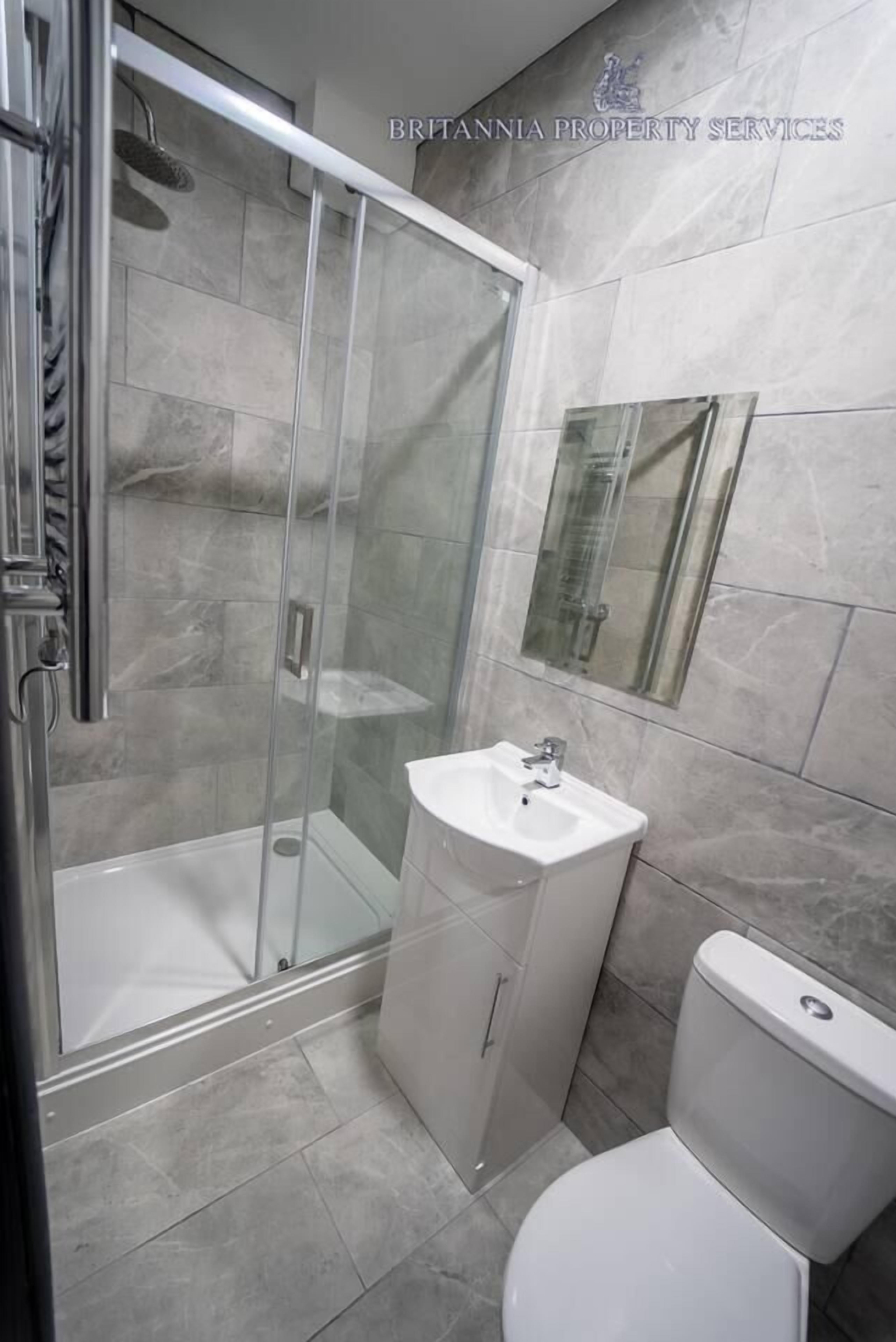 A modern bathroom with a glass-enclosed shower, a white sink, and a toilet.