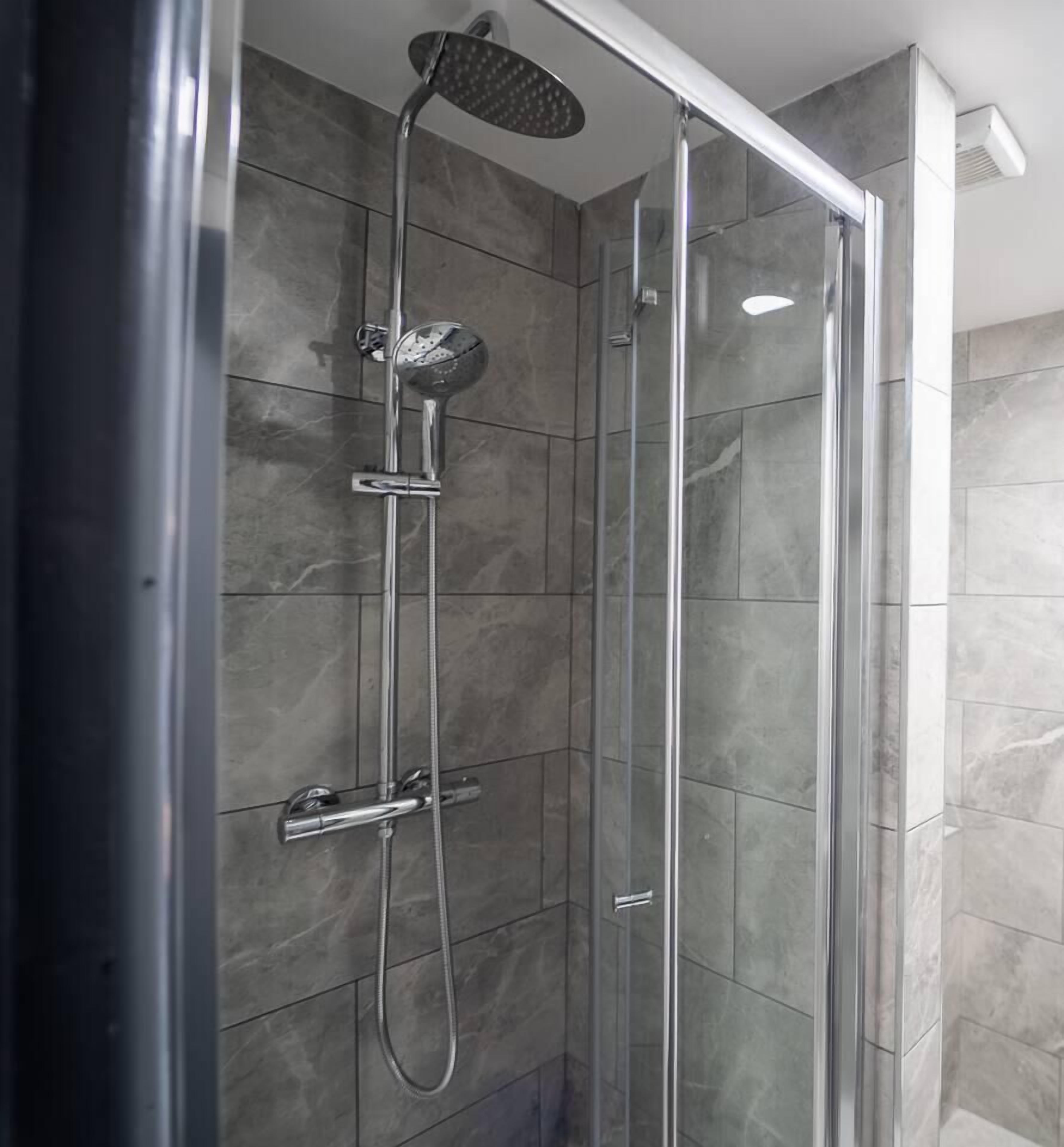 A glass-enclosed shower with a handheld showerhead and a wall-mounted control panel.
