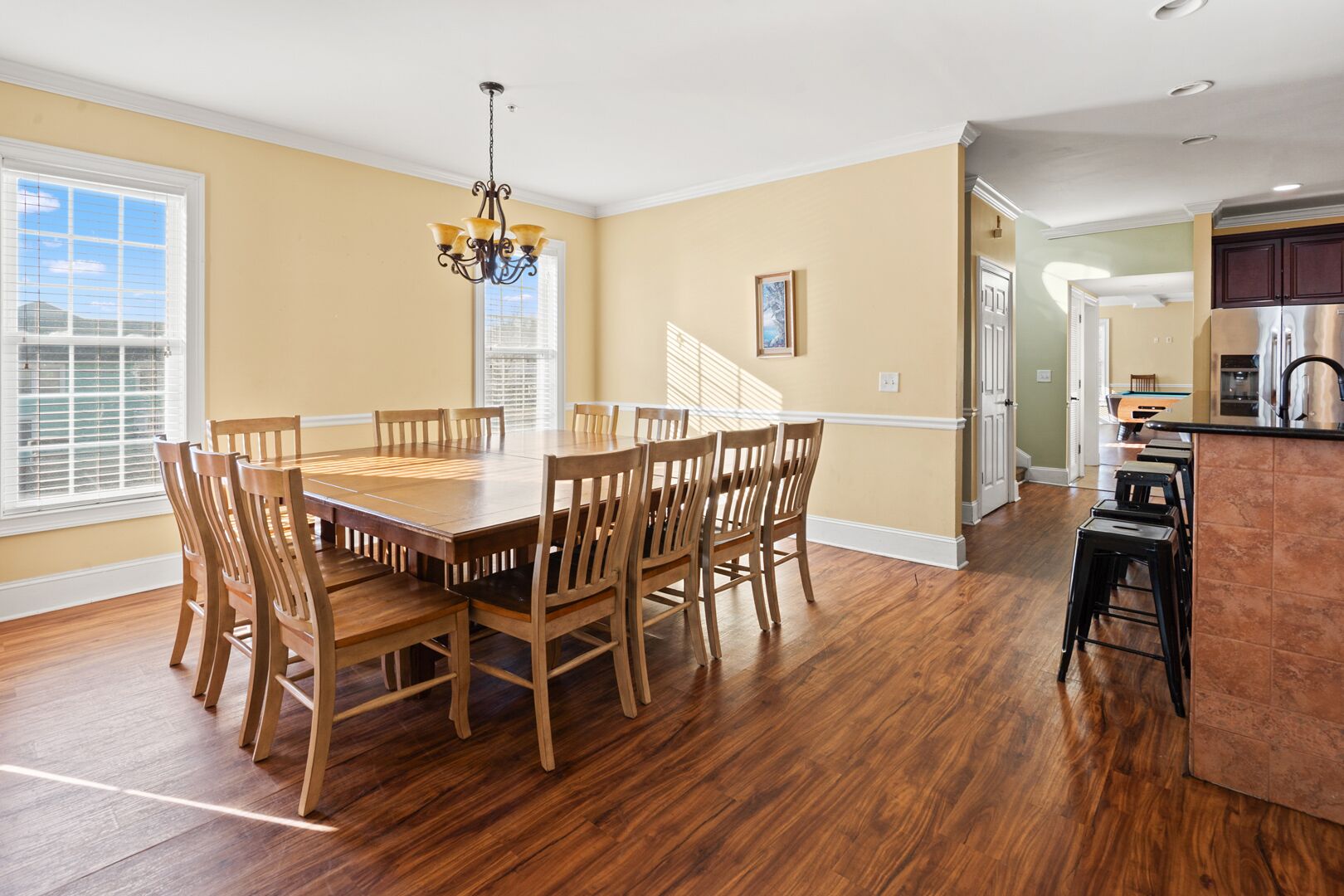 A dining room with a wooden table and chairs, a chandelier, and a view of the outside through a window with blinds.