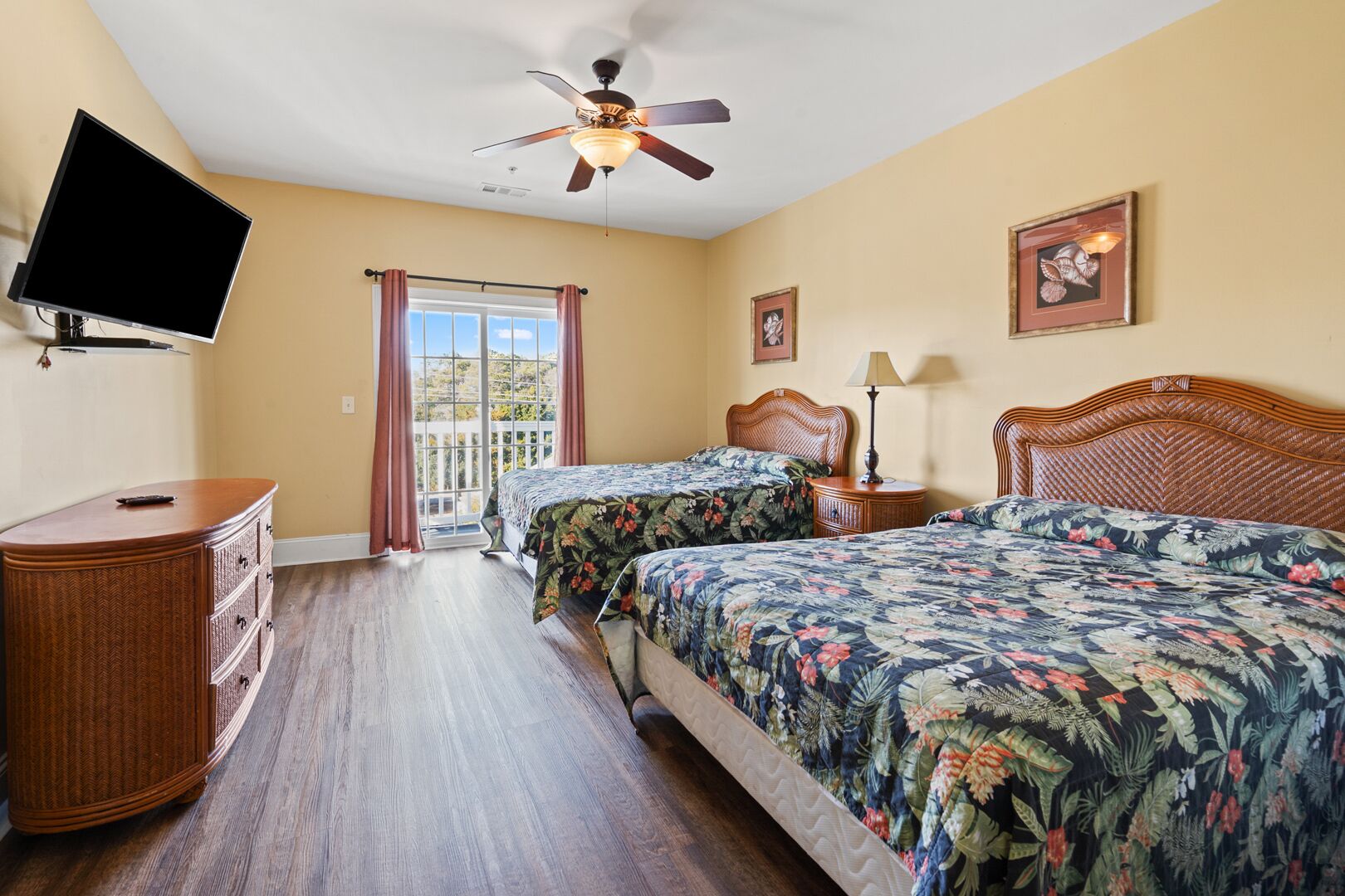 Une chambre avec deux lits, un ventilateur de plafond, une télévision, une commode et une fenêtre avec des rideaux.