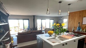 Eine moderne Küche mit einer zentralen Kochinsel, einem Geschirrspüler und einem Spülbecken. An der Decke hängen Lampen, auf der Insel steht eine Schüssel mit Zitronen und eine Vase mit Blumen.