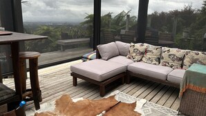 Ein moderner Außenbereich mit einer gepolsterten Couch, einer Holzterrasse und Blick auf die umliegende Landschaft.