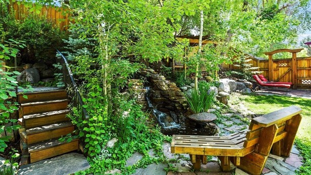 Un jardin avec un banc en bois, une petite cascade et une clôture en bois.