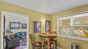 Un espace de vie compact comprenant un coin repas, un canapé, une petite table et une fenêtre ornée de vitraux.