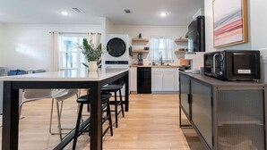 Cocina moderna con una isla central, taburetes de bar, microondas, tostadora y lavavajillas.
