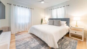 Un dormitorio con cama, mesitas de noche, ventilador de techo y cortinas.