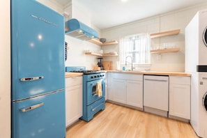 A kitchen with a blue refrigerator, white cabinets, a stove, and a dishwasher.